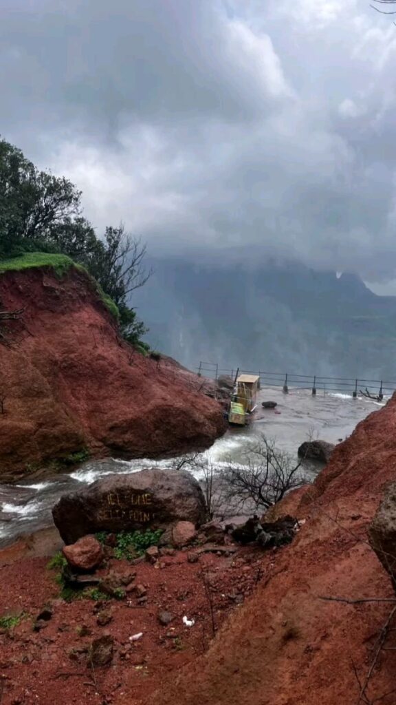 Matheran hill viewpoint with red rocky terrain, flowing water, and misty mountain views during monsoon