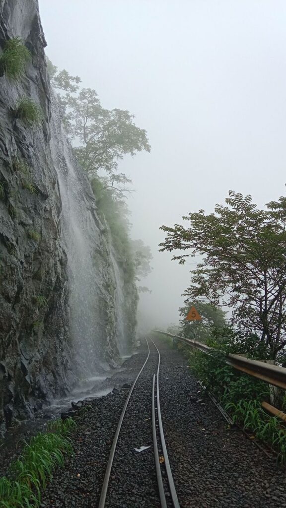 Matheran toy train railway track through misty hills with a waterfall and lush green monsoon landscape